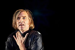 Nahaufnahme des Schauspielers Frank Siebenschuh, sprechend vor dunklem Hintergrund, Szene aus „Oinkonomy" am Theater Gütersloh